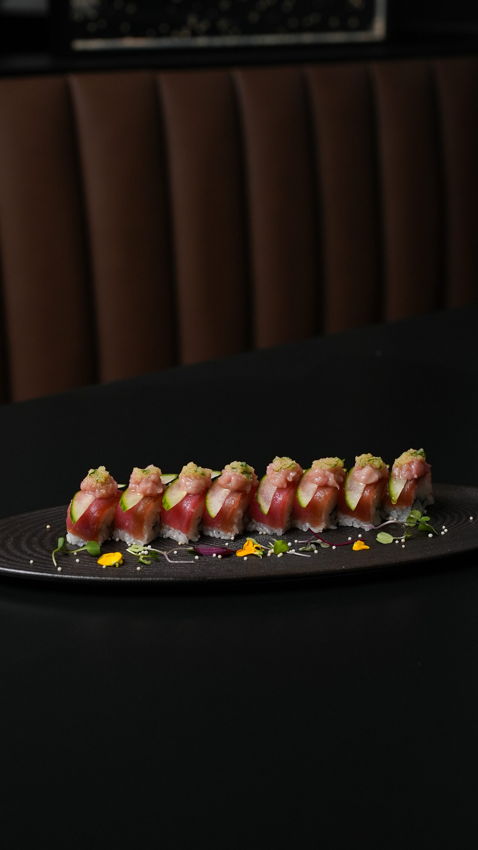 Tuna oshi sushi with cucumber and edible flowers on a black plate